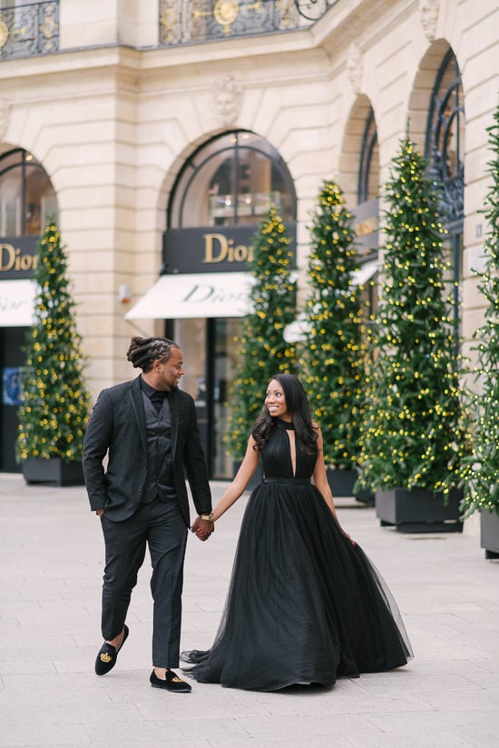 Cute couple walking holding in hands in front of Dior store in Place Vendome - beautiful Christmas decoration in the background Cute couple walking holding in hands in front of Dior store in Place Vendome - beautiful Christmas decoration in the background
